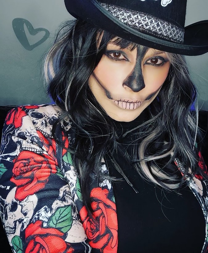 Maquillage de squelette avec nez noir allongé et dents dessinées, chapeau western noir et veste à roses rouges.
