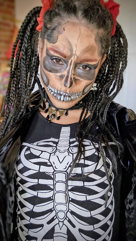 Maquillage de squelette aux tons bruns et orangés avec orbites sombres et dents détaillées, porté avec des tresses noires.