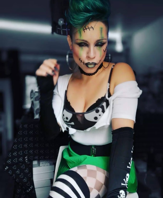 Maquillage vert et noir avec coutures dessinées, cheveux turquoise, tenue noire et blanche et jupe verte.