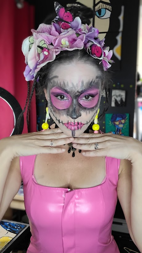 Maquillage de squelette gris aux yeux roses, lèvres roses et argentées, couronne de fleurs mauves et papillons.